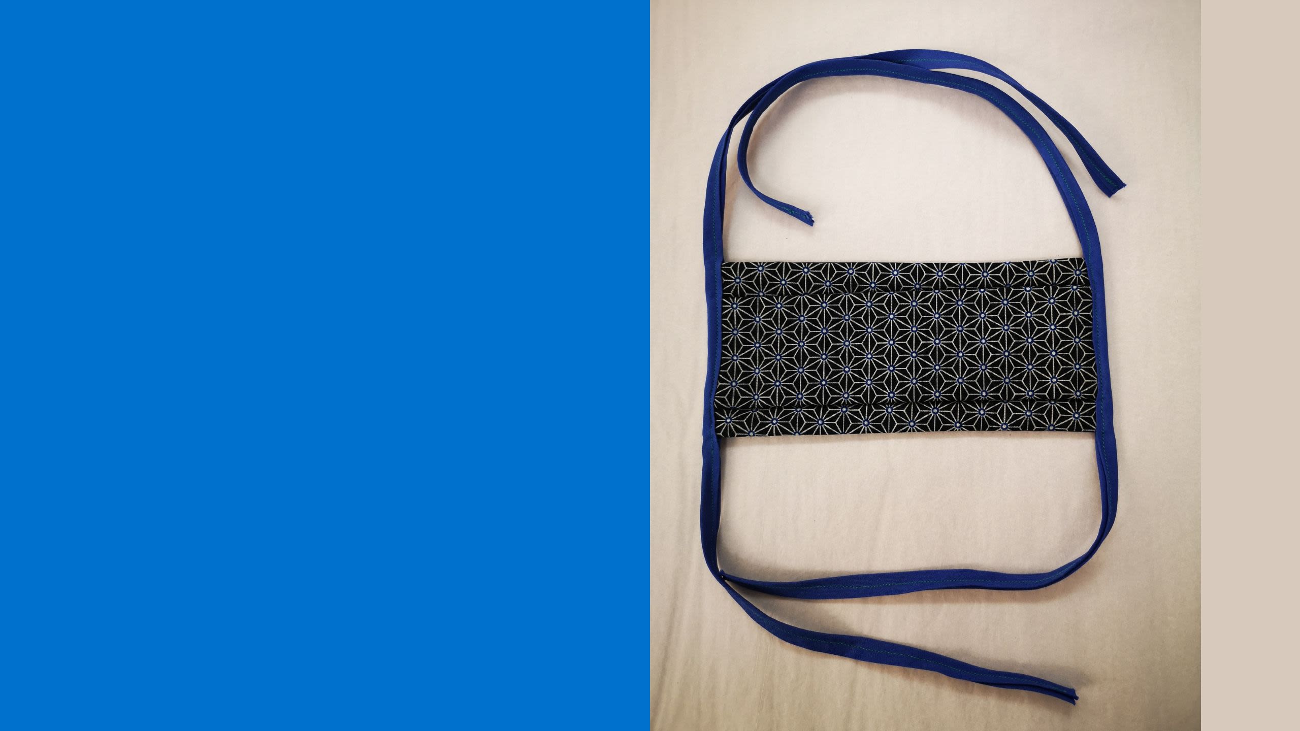 Handmade face covering of black patterned cotton with blue tie straps (Inv 18497)